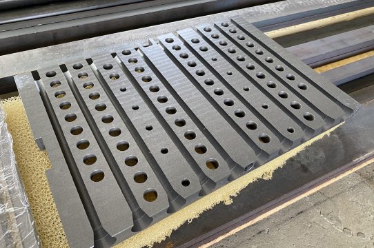 Sada kovových dílů s řadou přesně vyvrtaných otvorů z realizací 2KT